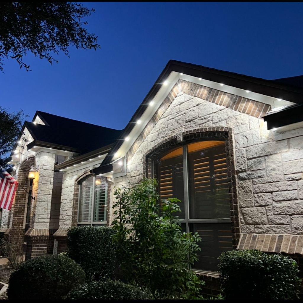 White permanent accent lighting along a stone home roofline at dusk