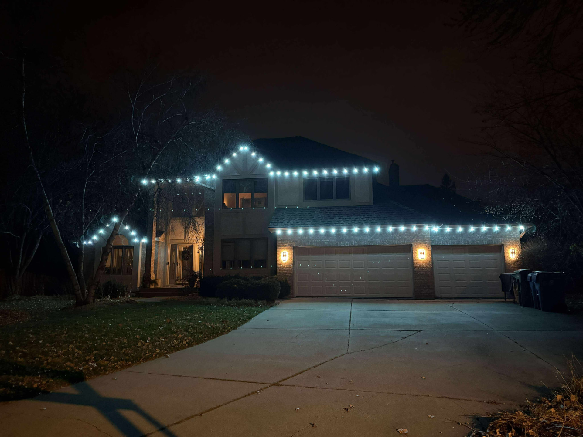 Cool-white roofline lighting on a home with a three-car garage